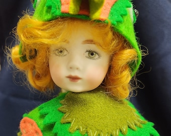 May include: A porcelain doll wearing a green and orange frog costume. The doll has long, curly red hair and a painted face with green eyes.