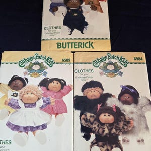 Könnte beinhalten: Drei Vintage-Butterick-Schnittmuster für Cabbage Patch Kids-Kleidung. Die Muster zeigen Illustrationen der Puppen in verschiedenen Outfits. Die Muster sind mit dem Text "CLOTHES For your Cabbage Patch Kids!" versehen.