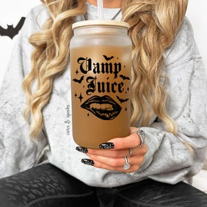 May include: A frosted glass reusable tumbler with a bamboo lid and a black and white graphic that says "Vamp Juice" with a vampire mouth and fangs. The tumbler is filled with a brown liquid and has a straw.