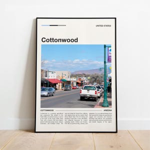 May include: A framed print showing a photograph of Cottonwood, Arizona, with the town's name in large black letters. The image depicts a street scene with cars, buildings, and a blue sky.