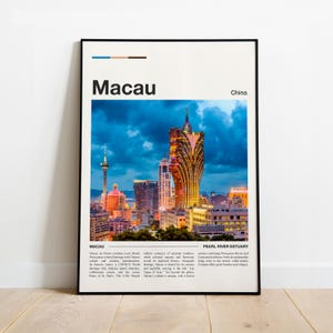 May include: A framed poster featuring a nighttime cityscape of Macau, China. The image showcases illuminated skyscrapers and buildings under a dark blue sky. The word "Macau" is prominently displayed at the top.