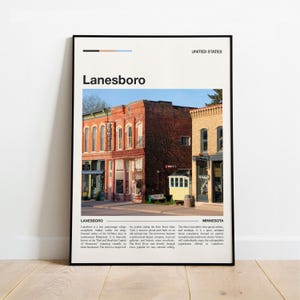 May include: A framed print featuring a photograph of Lanesboro, Minnesota, with the town's name at the top. The image shows historic brick buildings in various colors, with text at the bottom describing the town.