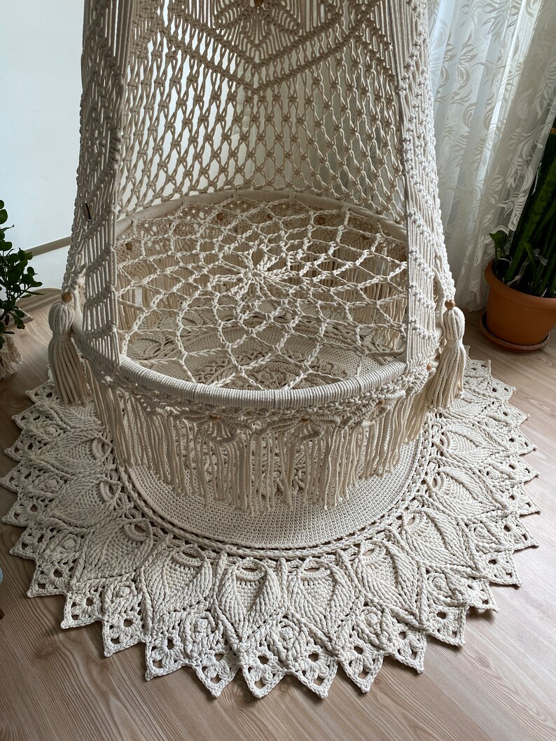 May include: A white macrame hanging chair with a round base and fringe details. The chair is suspended from the ceiling and has a woven design.