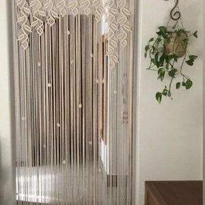 May include: A white macrame curtain with a leaf pattern hangs in a doorway. The curtain is made of cotton cord and has a natural, bohemian style.