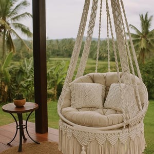 May include: A cream macrame hanging chair with two decorative cushions. The chair hangs from a wooden beam on a porch, with a small side table and a woven rug. The background shows green foliage.