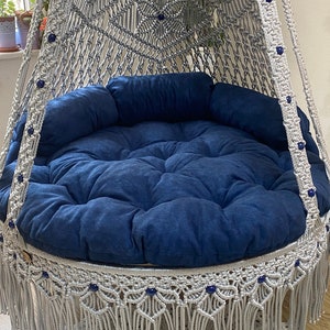 May include: A gray macrame hanging chair with a blue cushion and fringe trim. The chair is decorated with blue beads.