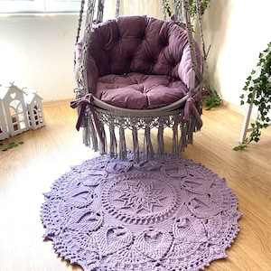 May include: A purple crocheted mandala rug with a gray hanging chair with a purple cushion in the background.