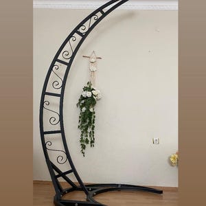 May include: A black metal archway with a decorative scroll design. The archway is curved and has a circular base. The archway is standing on a wooden floor.