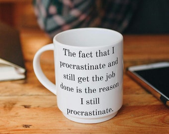May include: White coffee mug with a black text quote that reads "The fact that I procrastinate and still get the job done is the reason I still procrastinate."