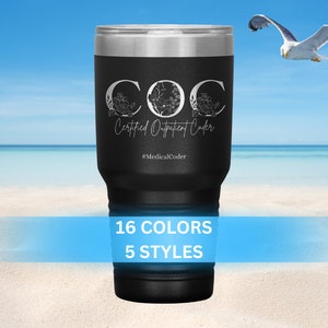 Peut inclure: Un gobelet en acier inoxydable noir avec un motif blanc qui dit "COC Certified Outpatient Coder #MedicalCoder". Le gobelet est sur une plage avec un ciel bleu et des nuages blancs en arrière-plan.