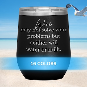 Puede incluir: Un vaso de vino de acero inoxidable negro con el texto "El vino puede que no resuelva tus problemas, pero el agua o la leche tampoco." El vaso está sentado en una playa de arena blanca con un cielo azul y el océano en el fondo. El texto "16 COLORES" está impreso debajo del vaso.