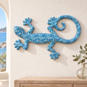 May include: A wall-mounted gecko sculpture featuring a vibrant blue and white paisley pattern. The lizard is depicted in a crawling position with its long tail curled into a circular shape, showcasing intricate floral and teardrop motifs.
