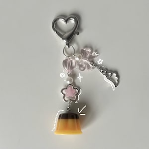 May include: A silver charm keychain with a pink flower, white beads, and a pink and brown pudding charm.