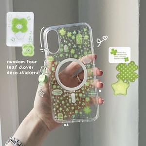May include: Clear phone case with a green four-leaf clover pattern and a white circular cutout. Includes a charm with green beads and a star. The text "random four leaf clover deco stickers!" is visible.