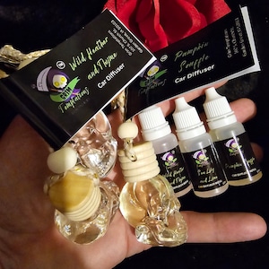 May include: Three glass skull car diffusers with wooden stoppers. The diffusers are labeled "Wild Heather and Thyme", "Sea Lily and Lime", and "Pumpkin Souffle".