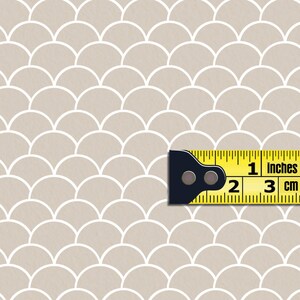 May include: A beige background with a white repeating pattern of overlapping half circles. A yellow measuring tape with black markings is placed on the pattern. The tape reads "1 inches" and "3 cm".