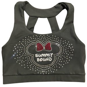 May include: Dark gray sports bra with a racerback design. The front features a rhinestone-studded Minnie Mouse head outline with a red bow and the text "SUMMIT BOUND" in white.