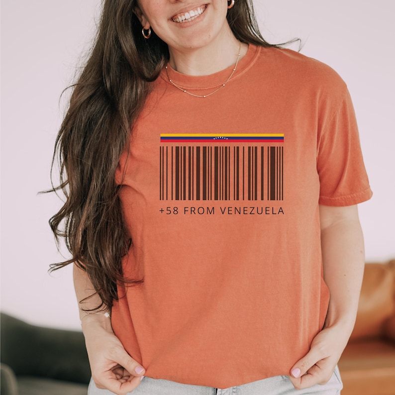 May include: Burnt orange t-shirt featuring a barcode design with the colors of the Venezuelan flag at the top. The text "+58 FROM VENEZUELA" is printed below the barcode. The shirt is a short-sleeved, casual style.