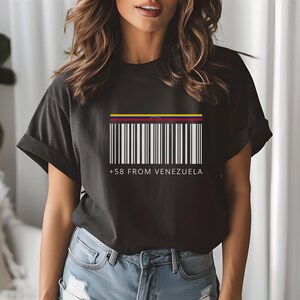 May include: Black t-shirt featuring a barcode design with the colors of the Venezuelan flag at the top. The text "+58 FROM VENEZUELA" is printed below the barcode. The shirt is a casual wear item.