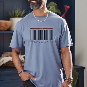 May include: A light blue t-shirt featuring a barcode design with the colors of the Venezuelan flag at the top. Below the barcode, the text reads "+58 FROM VENEZUELA". The shirt is a casual wear item.