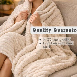 May include: A cream-colored, textured blanket draped over a person seated on a sofa. The blanket has a ribbed pattern and the text "Quality Guarantee", "100% polyester", and "Lightweight and soft".