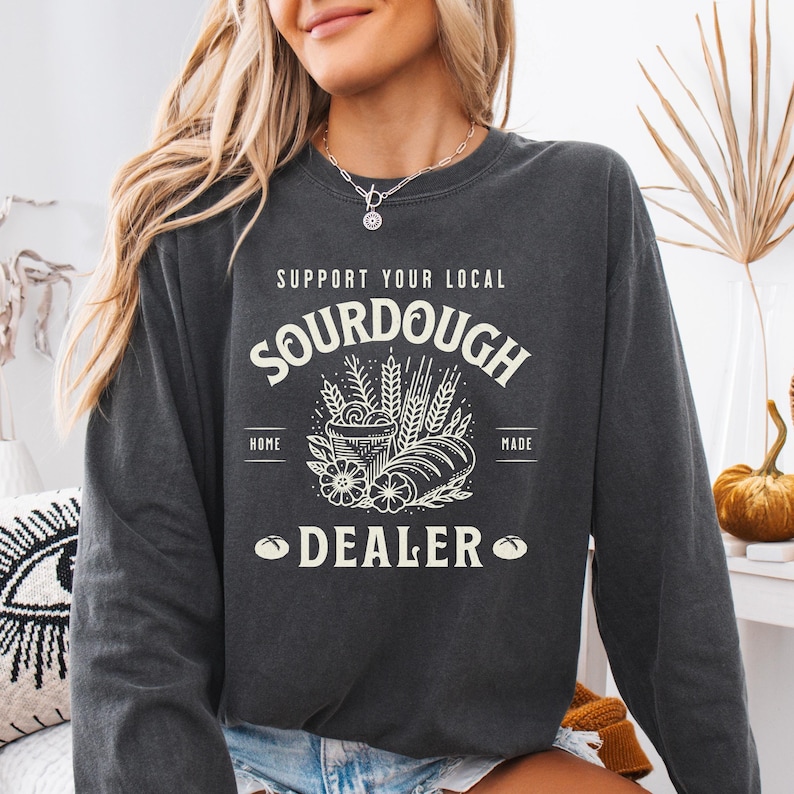K&ouml;nnte beinhalten: Ein dunkelgrauer Langarmsweatshirt mit einem wei&szlig;en Grafikdesign, auf dem "Support Your Local Sourdough Home Made Dealer" steht, mit einer Zeichnung eines Laibes Brot, Weizen und einer Sch&uuml;ssel Teig.