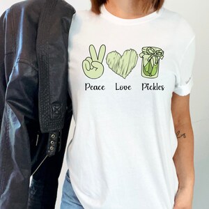 May include: White t-shirt with a green peace sign, a heart, and a jar of pickles. The text "Peace Love Pickles" is printed below the images.
