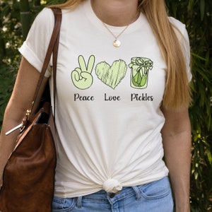 May include: White t-shirt with a green peace sign, heart, and jar of pickles. The text "Peace Love Pickles" is printed below the images.