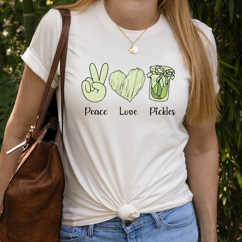 May include: White t-shirt with a green peace sign, heart, and jar of pickles. The text "Peace Love Pickles" is printed below the images.