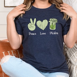 May include: A navy blue t-shirt with a peace sign, heart, and jar of pickles graphic. The text "Peace Love Pickles" is printed below the graphic.