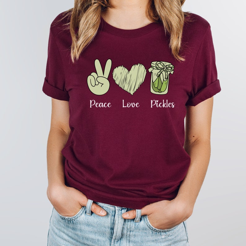 May include: A maroon t-shirt with a peace sign, heart, and jar of pickles graphic. The text "Peace Love Pickles" is printed below the graphic.