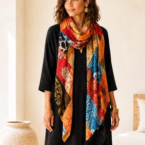 May include: A long rectangular scarf featuring a vibrant patchwork design with various geometric and floral patterns in shades of red, orange, blue, and black. The scarf is draped over a solid black dress with three-quarter length sleeves.