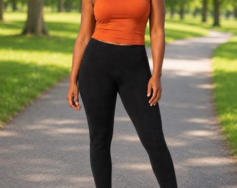 May include: A rust-colored sleeveless tank top with a scoop neckline paired with solid black leggings and blue and white athletic sneakers. The tank top is cropped at the waist, and the leggings are full-length, fitted, and feature a simple design.