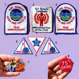 May include: A collection of vintage Girl Scout and game patches. Patches include text such as "Girl Scouts Going and Growing", "70th Anniversary", "Game Night", and bowling-themed patches. The patches are in various shapes and colors.