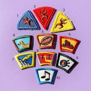 May include: A collection of embroidered patches in various shapes and colors. Designs include a running figure, a football, a car, a deer, a music note, and other symbols. Each patch has a detailed, stitched design.