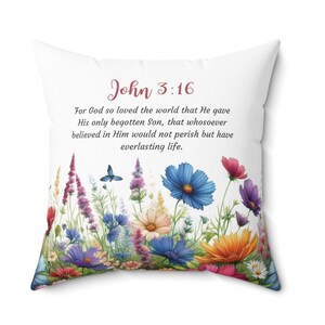 May include: White square throw pillow with a floral design at the bottom and the text "John 3:16" in red script. The floral design includes blue, purple, orange, and red flowers. The text "For God so loved the world..." is printed below.