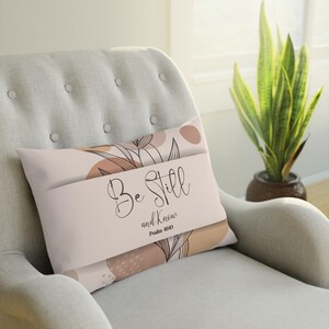 Puede incluir: Una almohada beige con un diseño floral y el texto "Be Still and Know" con el versículo "Salmo 46:10".