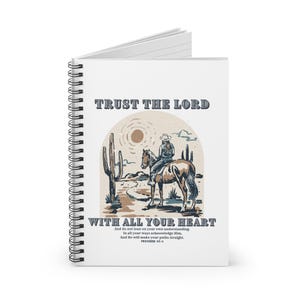 Puede incluir: Una libreta espiral blanca con un vaquero montando un caballo en un paisaje desértico. La libreta tiene el texto "TRUST THE LORD WITH ALL YOUR HEART" y un versículo bíblico de Proverbios 25-4.
