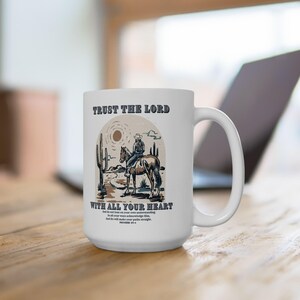 May include: White ceramic mug with a cowboy riding a horse in a desert landscape. The mug has the text "Trust the Lord with all your heart" and a bible verse.