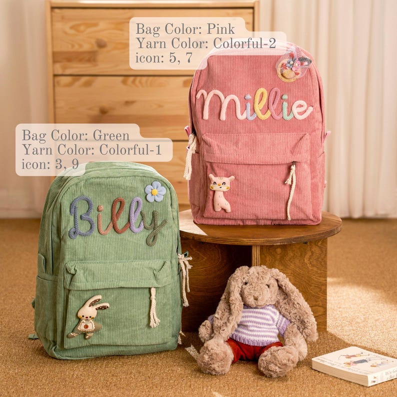 Op de afbeelding: Twee corduroy rugzakken, &eacute;&eacute;n roze en &eacute;&eacute;n groen, met gepersonaliseerde namen in kleurrijk garen. De roze rugzak zegt "Millie" en de groene rugzak zegt "Billy". Elke rugzak heeft decoratieve applicaties en een voorvak. Een knuffelkonijn en een boek staan ook op de foto.