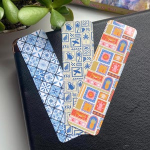 May include: Three colorful bookmarks with different patterns. The first bookmark has a blue and white tile pattern. The second bookmark has a yellow background with a blue, orange, and pink geometric pattern. The third bookmark has a white background with a blue, orange, and pink geometric pattern.