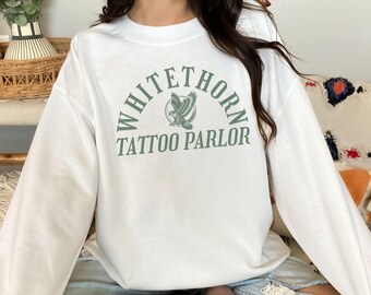 May include: White sweatshirt with a green graphic of an eagle and the text "Whitethorn Tattoo Parlor" in an arch.