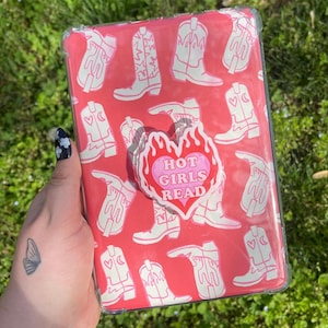 May include: A clear pink and white case for a tablet with a white cowboy boot pattern. A pink heart-shaped sticker with the text "Hot Girls Read" is attached to the case.