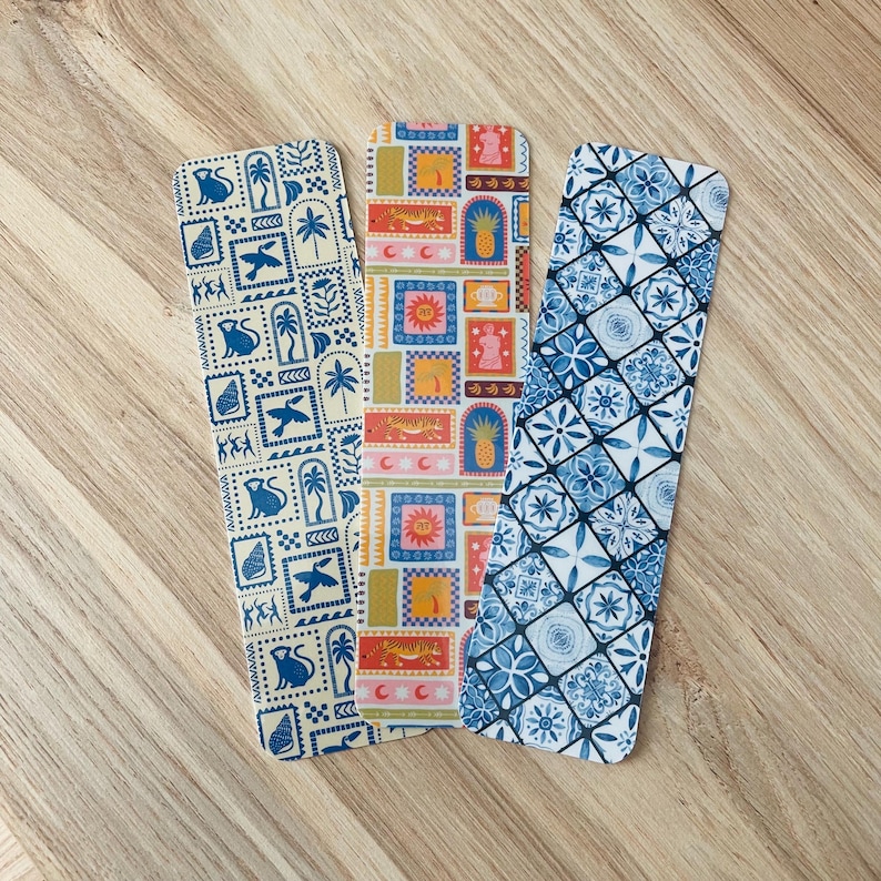 May include: Three colorful bookmarks with different patterns. The first bookmark has a white background with blue and yellow geometric shapes and animals. The second bookmark has a white background with orange, yellow, and blue geometric shapes and animals. The third bookmark has a white background with blue and white geometric shapes.