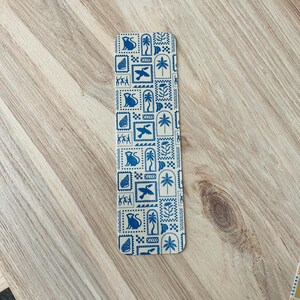 May include: A blue and white bookmark with a repeating pattern of monkeys, birds, palm trees, and geometric shapes.