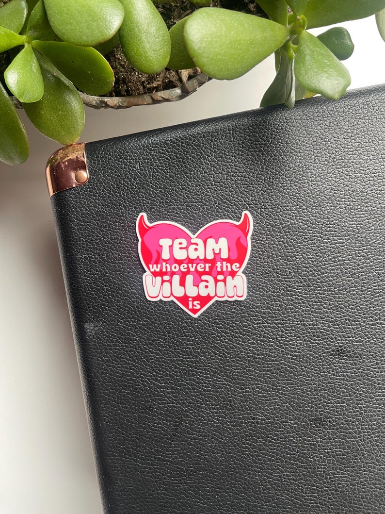 May include: Pink heart-shaped sticker with devil horns and the text "Team whoever the Villain is".
