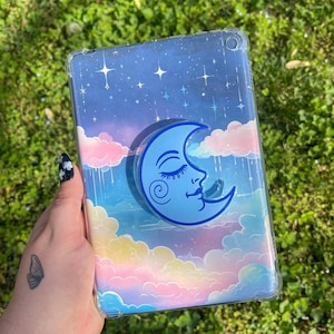 May include: A clear phone case with a blue and white moon design. The case has a starry night sky background with clouds and a rainbow effect.