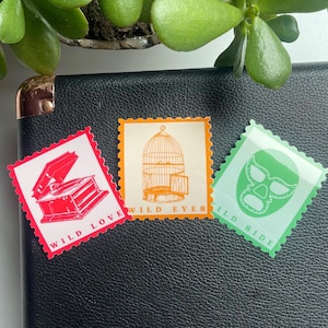 May include: Three colorful stickers with a vintage record player, a birdcage, and a wrestling mask. The stickers have a postage stamp design and include the text "Wild Love", "Wild Eyes", and "Wild Side".