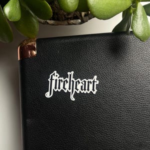 May include: A black leather notebook with a white sticker that says "fireheart" in a gothic font.