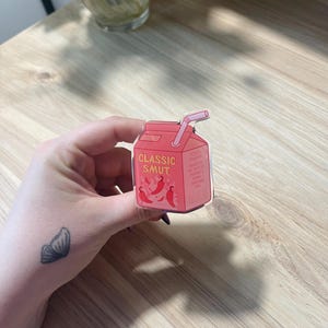 May include: A red and white cartoon illustration of a juice box with a straw. The juice box has the words "CLASSIC SMUT" printed on it and a few red chili peppers around the text.